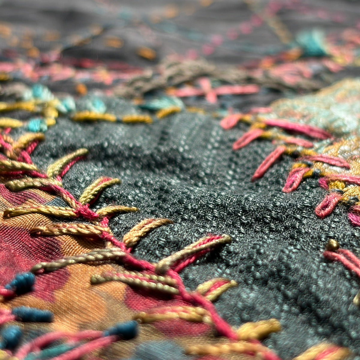 Close-up of a textured black fabric with colorful embroidered details in pink, gold, teal, and red.