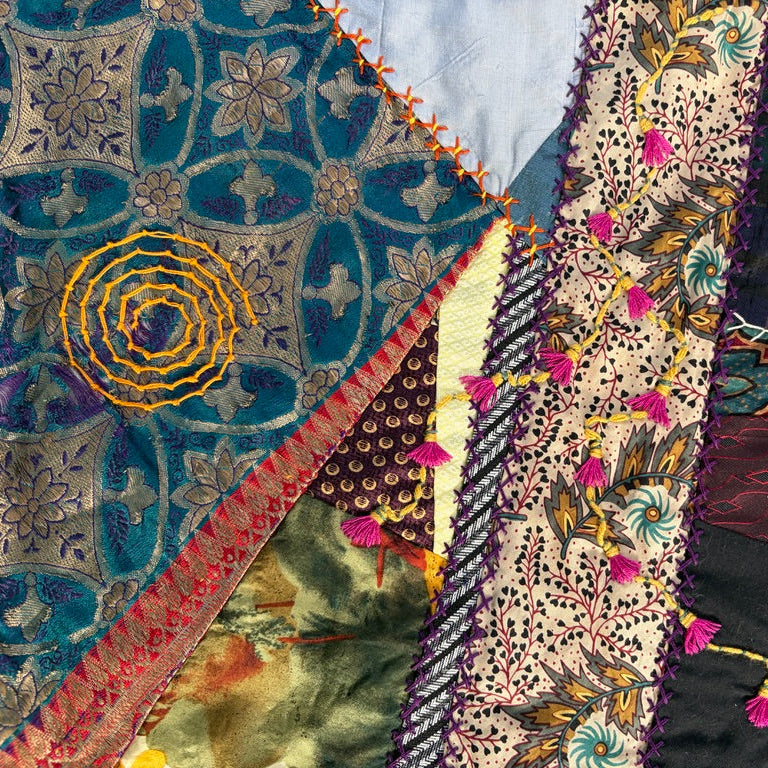 A close-up of a colorful patchwork quilt with multiple fabric panels, intricate embroidery, floral patterns, and decorative stitching.