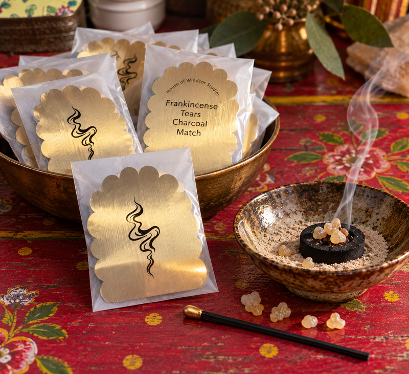 Frankincense Ritual Kits in a brass bowl, fancy long, black match with a gold tip and a lit charcoal tablet on sand in a ceramic bowl.