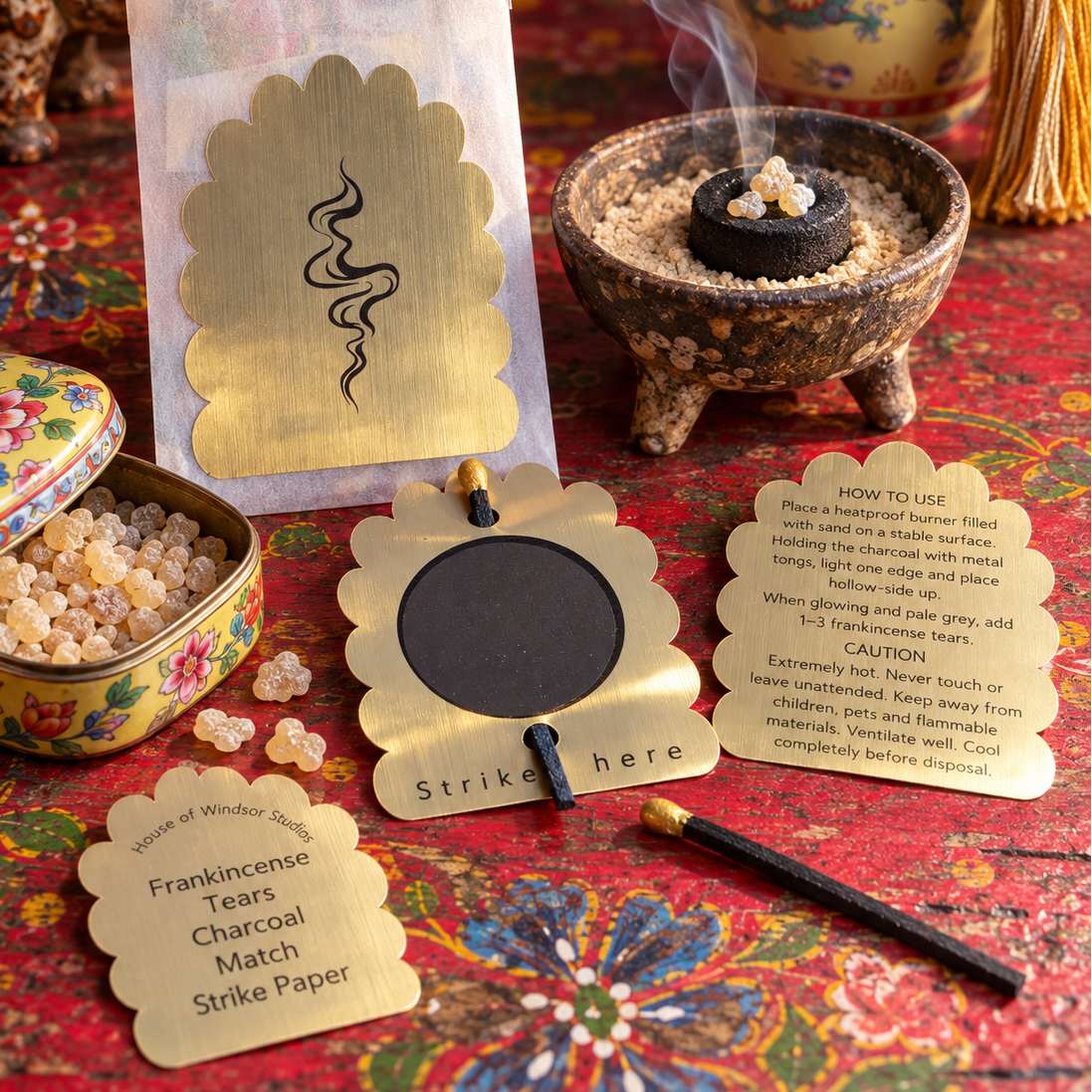 Frankincense Ritual Kit contents, and a lit charcoal tablet in a ceramic dish with sand, on a red painted table with an open box of frankincense tears, and interesting objects .